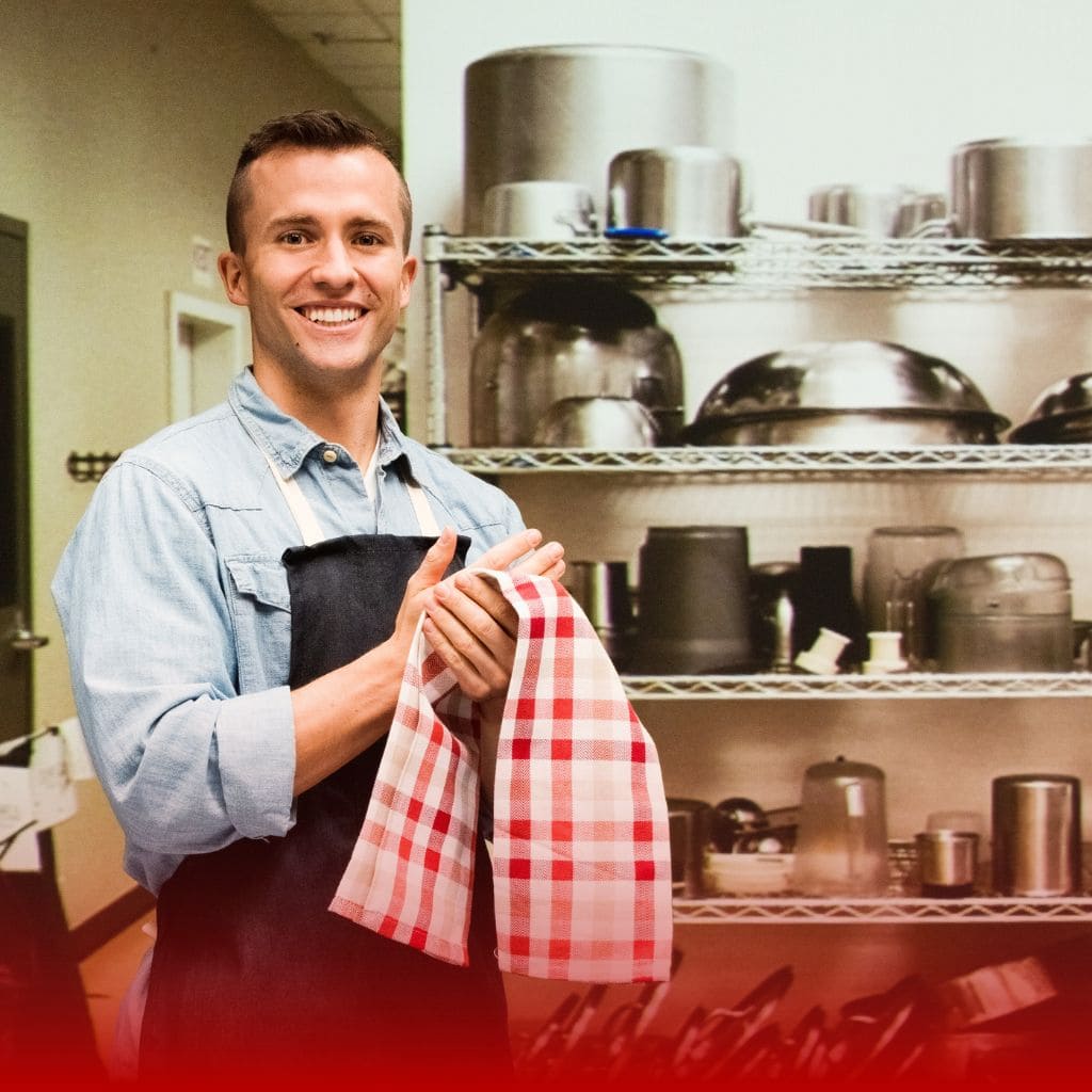 Catering & Food category. Young male chef in kitchen holding a red and white towel.